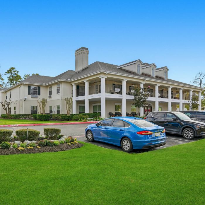 Two-story white Cypresswood homes with columns, landscaped lawn, and parked cars on a sunny day.
