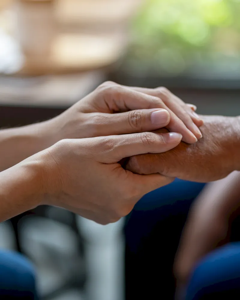 Two people sitting close, gently holding hands in a comforting and supportive gesture.