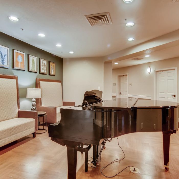 A black grand piano sits in a cozy room at The Terraces at Kingwood, featuring bench seating, artwork, and wood flooring.