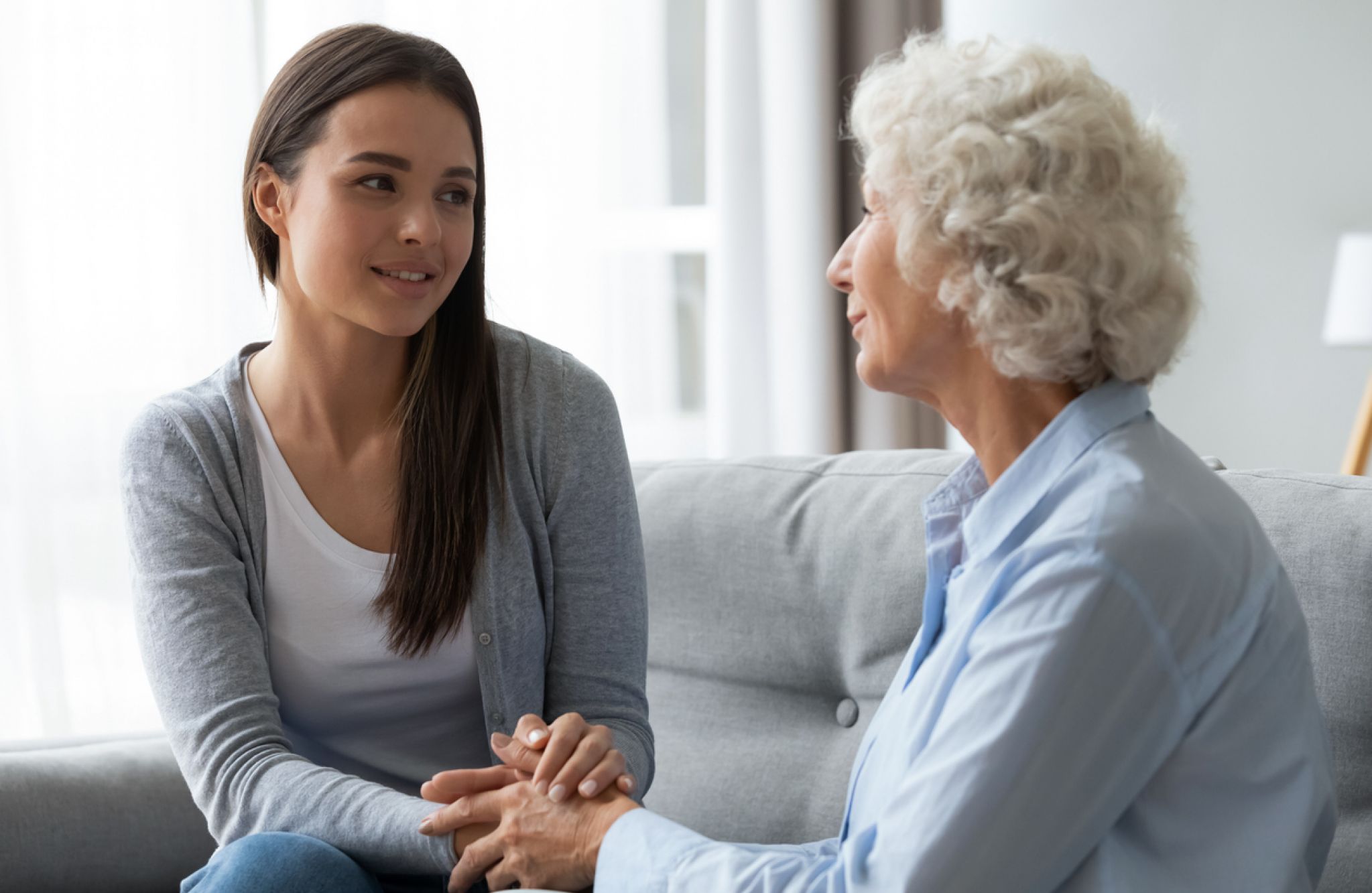 Younger woman holding an older woman's hands while they sit across from each other at a kitchen table