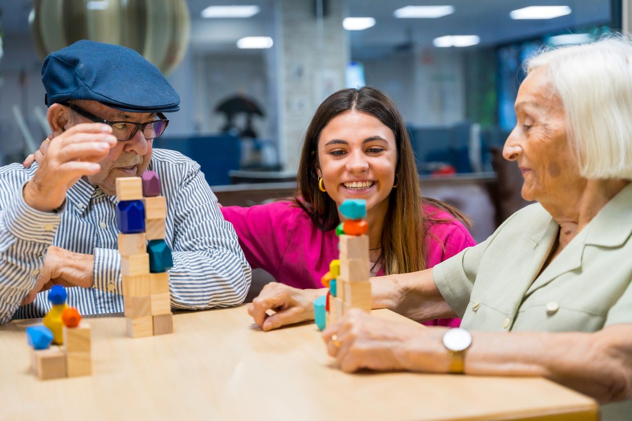 An elderly couple plays a game with blocks with their caregiver in a memory care community.